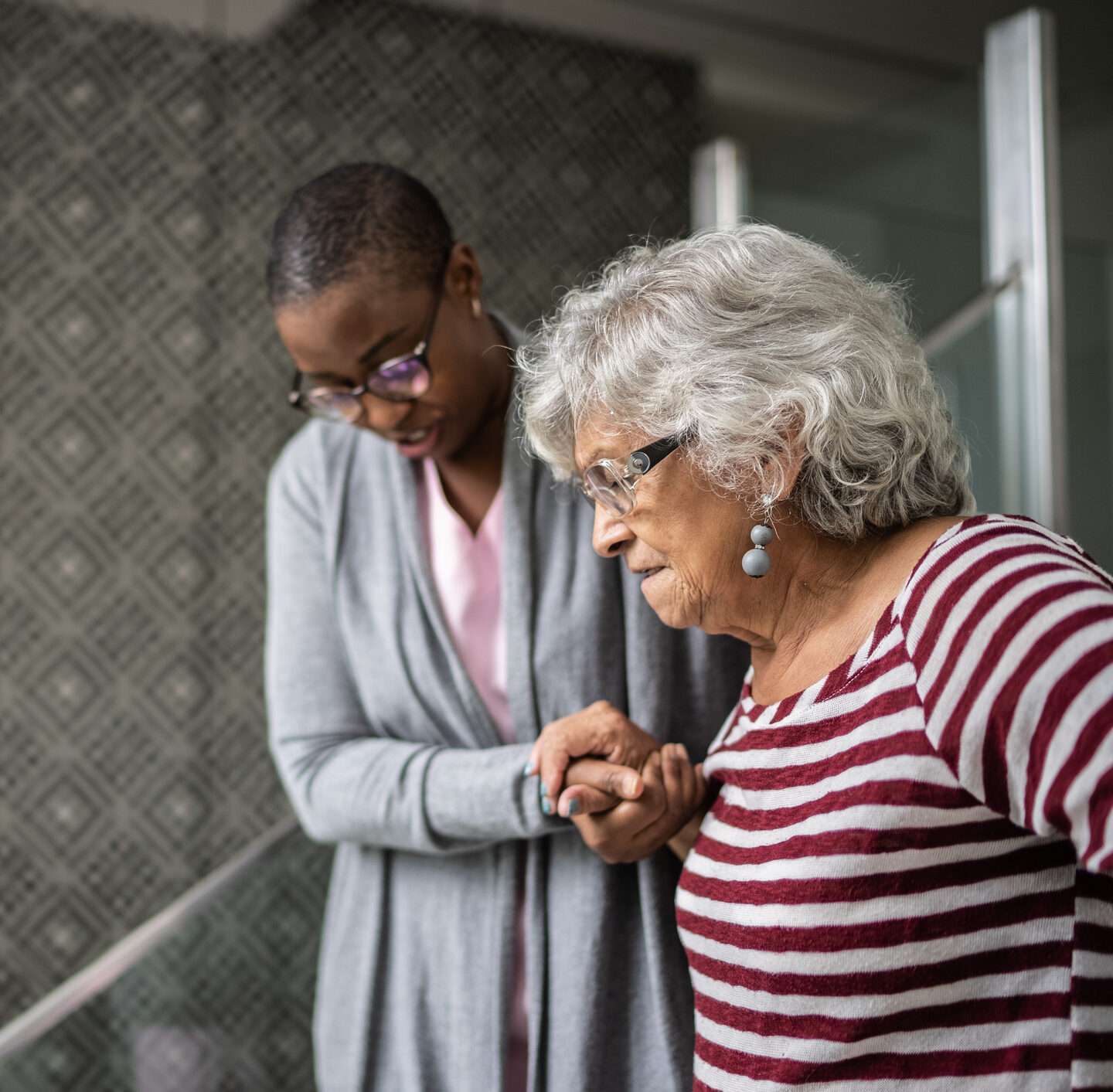 A caregiver helps a senior woman down the stairs in her home.